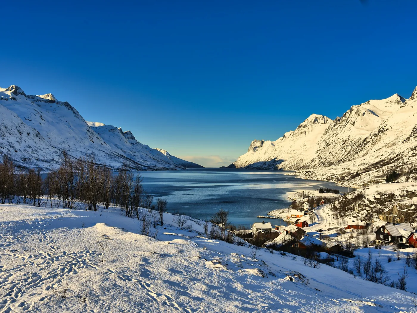 Zasněžené hory kolem fjordu nedaleko Tromsø pod temnou oblohou