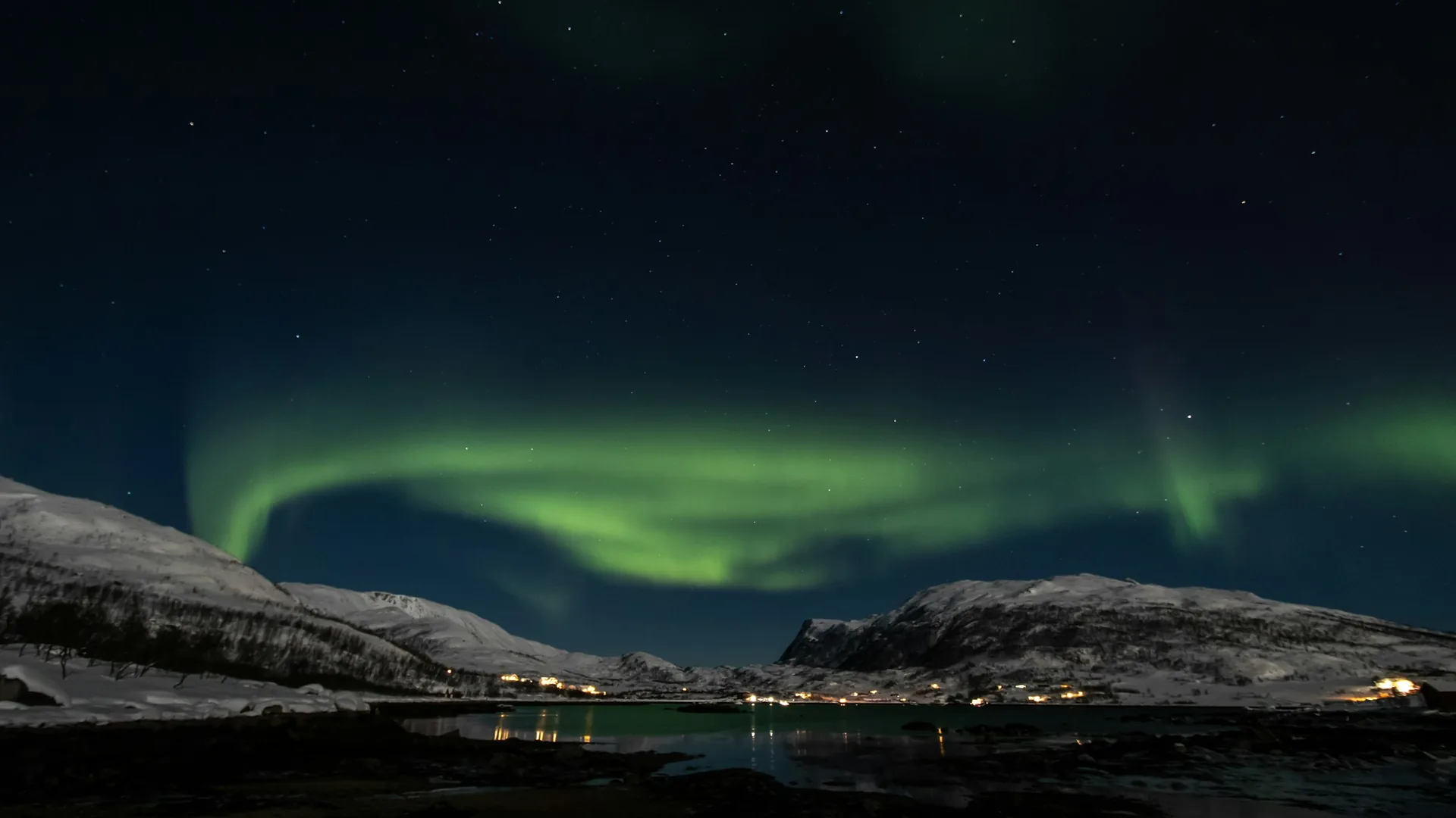 Zelená polární záře vířící nad zasněženým fjordem poblíž Tromsø, Norsko